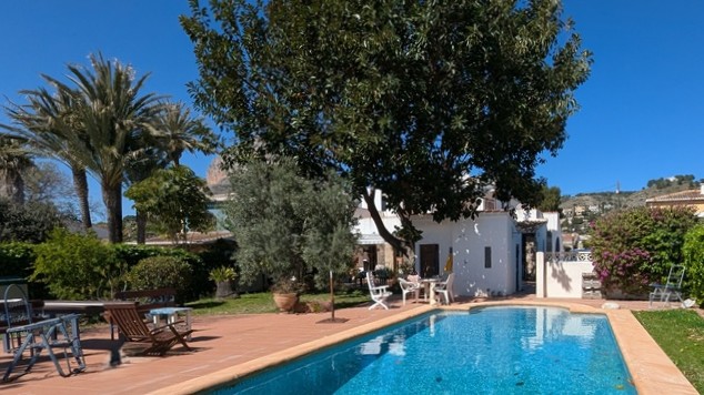 Privater rechteckiger Pool mit Terrakotta-Umrandung, eingebettet in einen eingewachsenen Garten mit Palmen und Blick auf das Montgó-Massiv.