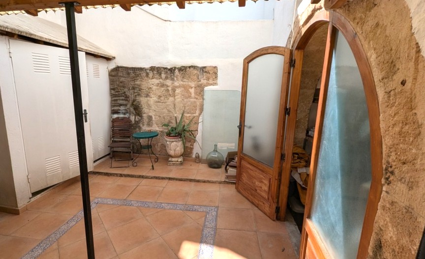 Traditioneller Innenhof mit freigelegten Tosca-Steinwänden, Terrakottaböden mit Zierborten und bogenförmigen Holztüren, die ins Innere führen.