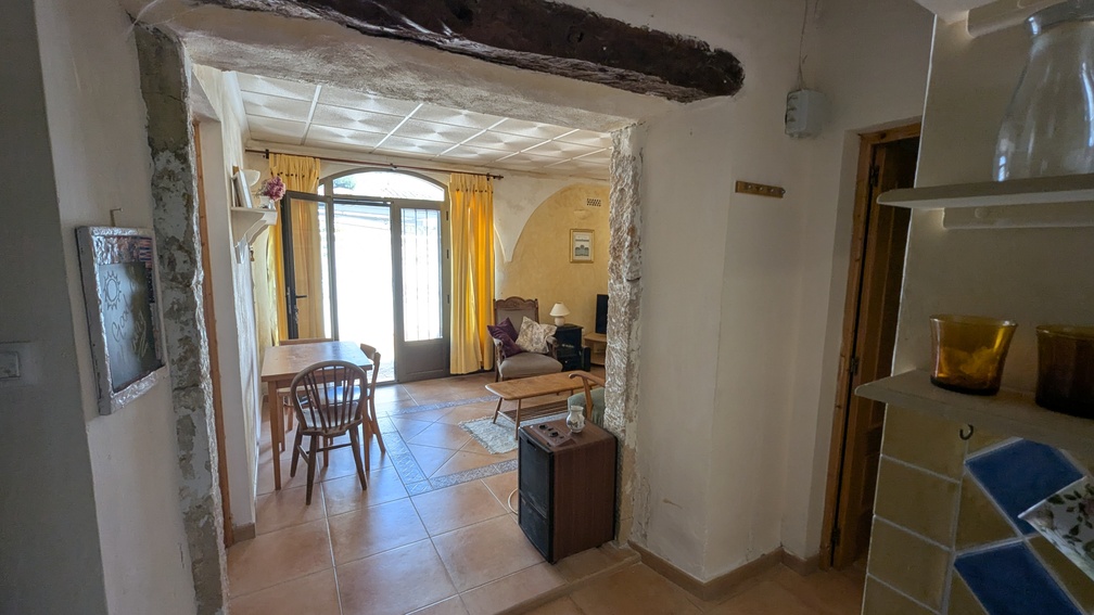 Traditioneller Tosca-Steinbogen mit dunklem Holzbalken, der in einen hellen Wohnbereich mit Terrakottafliesen und Rundbogentüren führt.