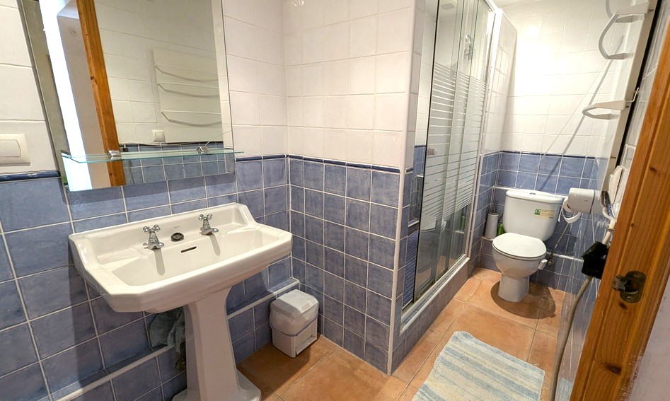 Traditionelles Badezimmer mit blau-weißen Wandfliesen, klassischem Säulenwaschbecken, Terrakottaboden und einer Dusche mit Glaskabine.