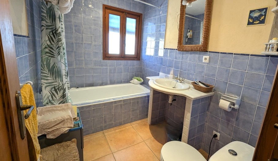 Traditionelles Badezimmer mit blauen Wandfliesen, Einbaubadewanne und Marmorwaschtisch. Terrakottaböden und ein Holzfenster unterstreichen den rustikalen Stil.