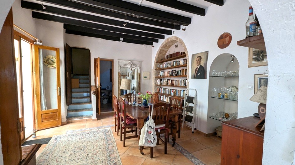 Traditionelles Esszimmer mit dunklen Deckenbalken, einem Einbauregal im Tosca-Steinbogen und Terrakottaböden neben einer gefliesten Treppe.