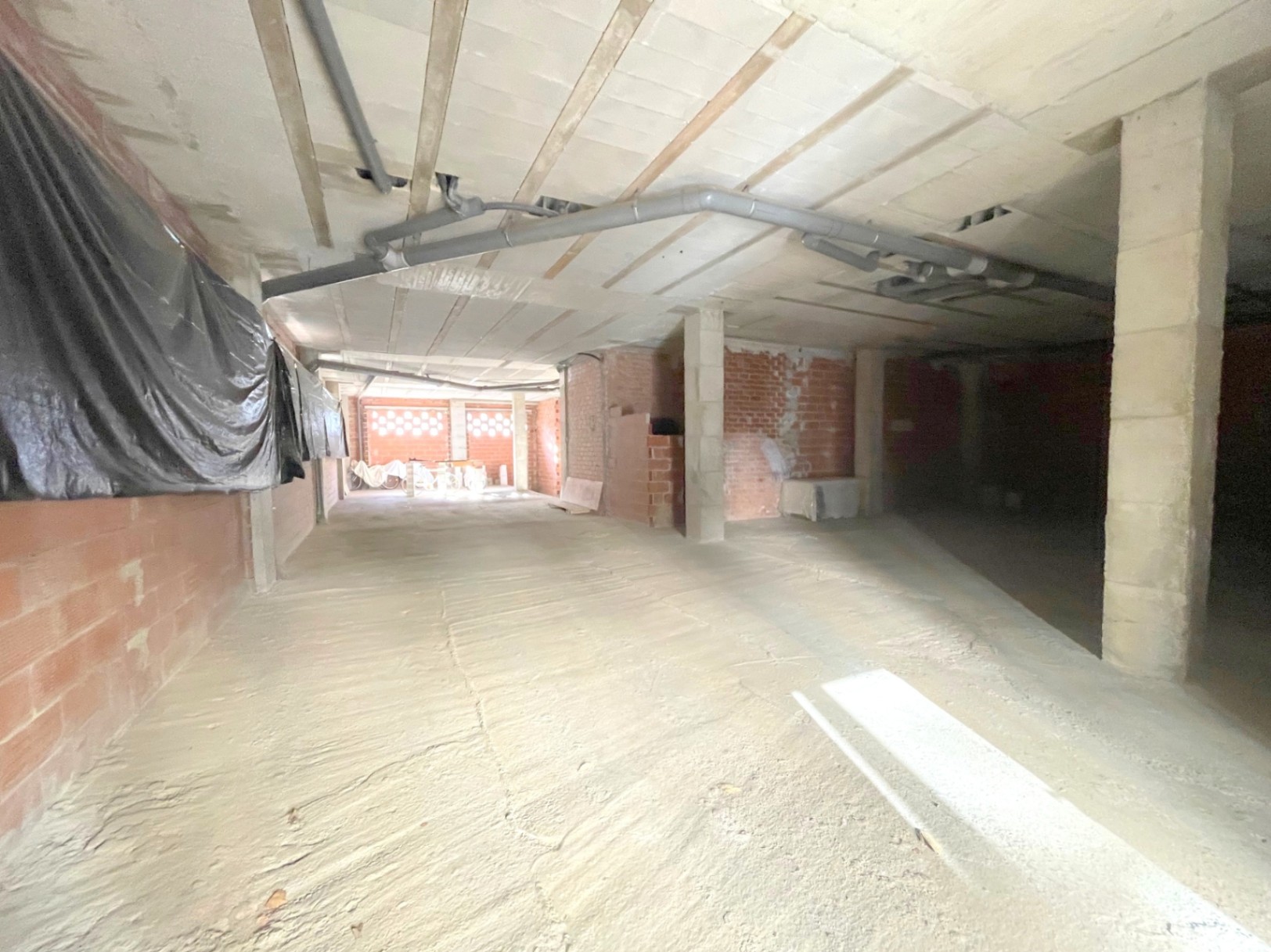 Offene Gewerbefläche im Rohbau mit Betonsäulen, sichtbaren Deckenrohren und Ziegelwänden, die eine flexible Gestaltung des Innenraums ermöglichen.