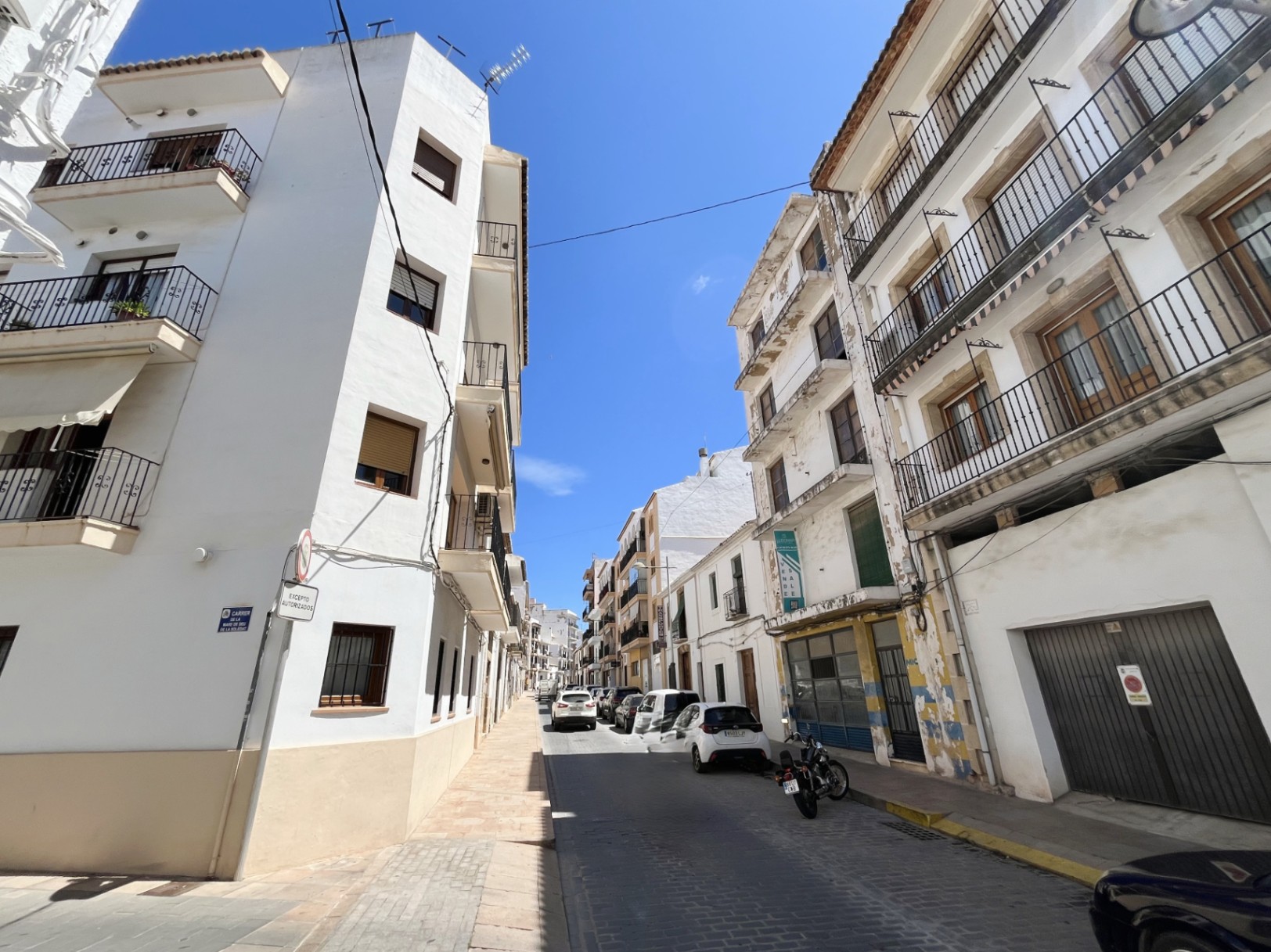 Außenansicht des vierstöckigen Gebäudes im Stadtzentrum von Jávea mit weißer Fassade, schmiedeeisernen Balkonen und einer großen Gewerbefläche im Erdgeschoss.