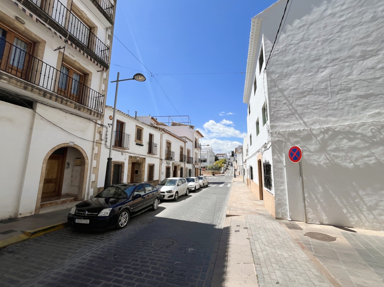 Außenfassade des Gebäudes in einer gepflasterten Straße der Altstadt von Jávea, mit traditionellen Tosca-Steinbögen und schmiedeeisernen Balkonen.