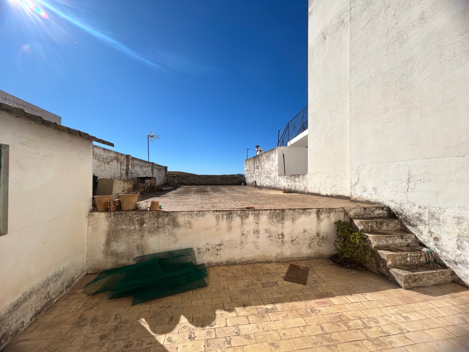 Mehrstöckige Dachterrasse mit Fliesenboden und Betontreppe, umgeben von weißen Mauern, ideal als großzügiger Außenbereich zum Renovieren.