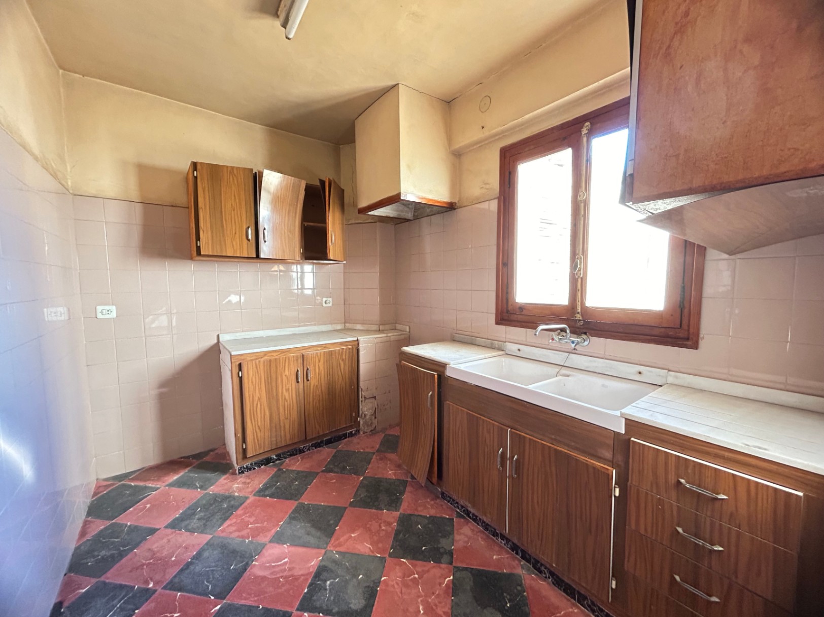 Originale Küche mit rot-schwarz schachbrettartigen Fliesen, Holzschränken und weißer Marmorarbeitsplatte. Ausgestattet mit Doppelspülbecken und Holzfensterrahmen.