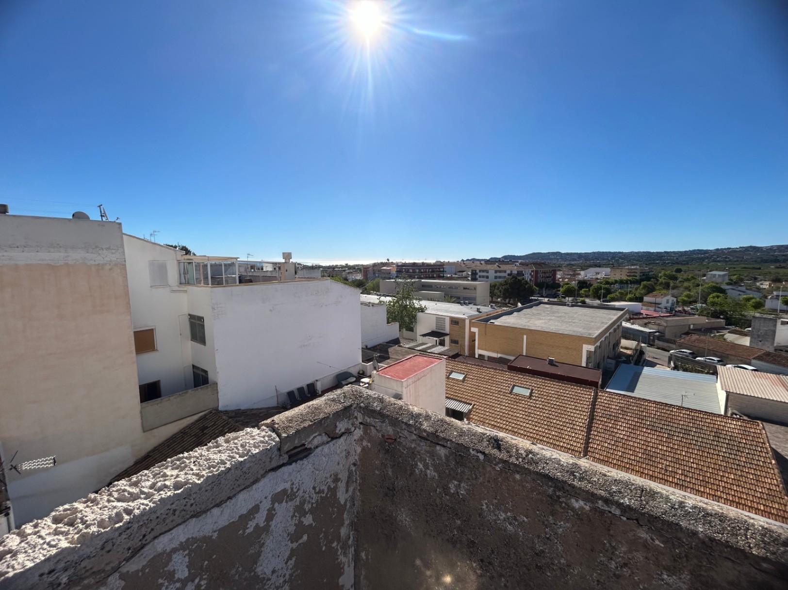 Panoramablick von der Dachterrasse über das Stadtzentrum von Jávea bis zum Mittelmeer, mit traditionellen Ziegeldächern und fernen Bergsilhouetten unter klarem Himmel.