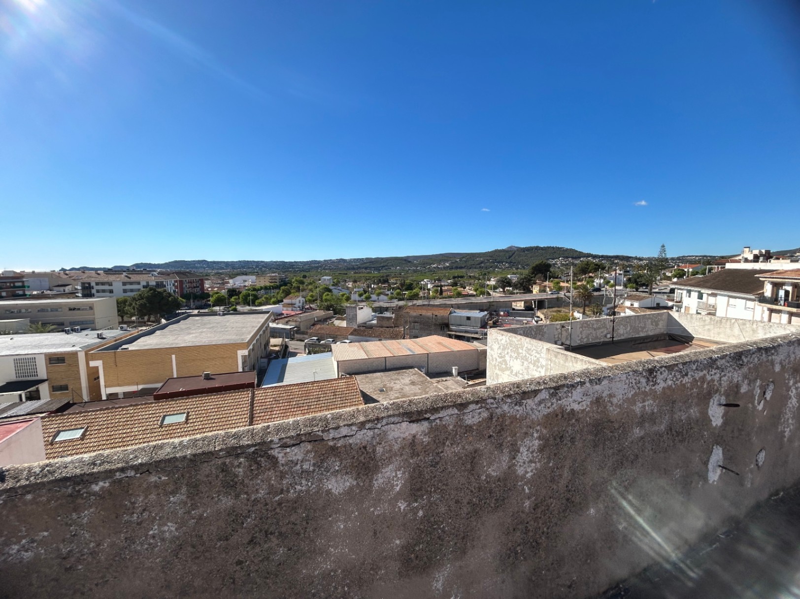 Panoramablick von der gemeinschaftlichen Dachterrasse über die Stadt Jávea und die angrenzenden grünen Hügel unter einem strahlend blauen Himmel.