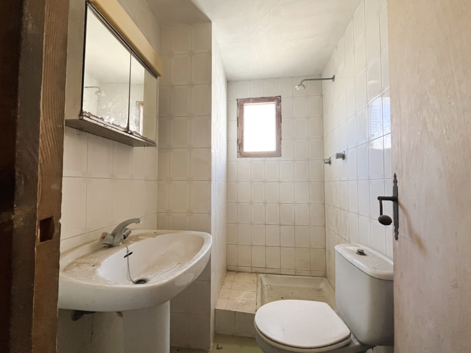 Funktionales Badezimmer mit weißen Fliesen, Standwaschbecken und Duschbereich mit kleinem Fenster. Ein Raum mit großem Potenzial für eine Modernisierung.
