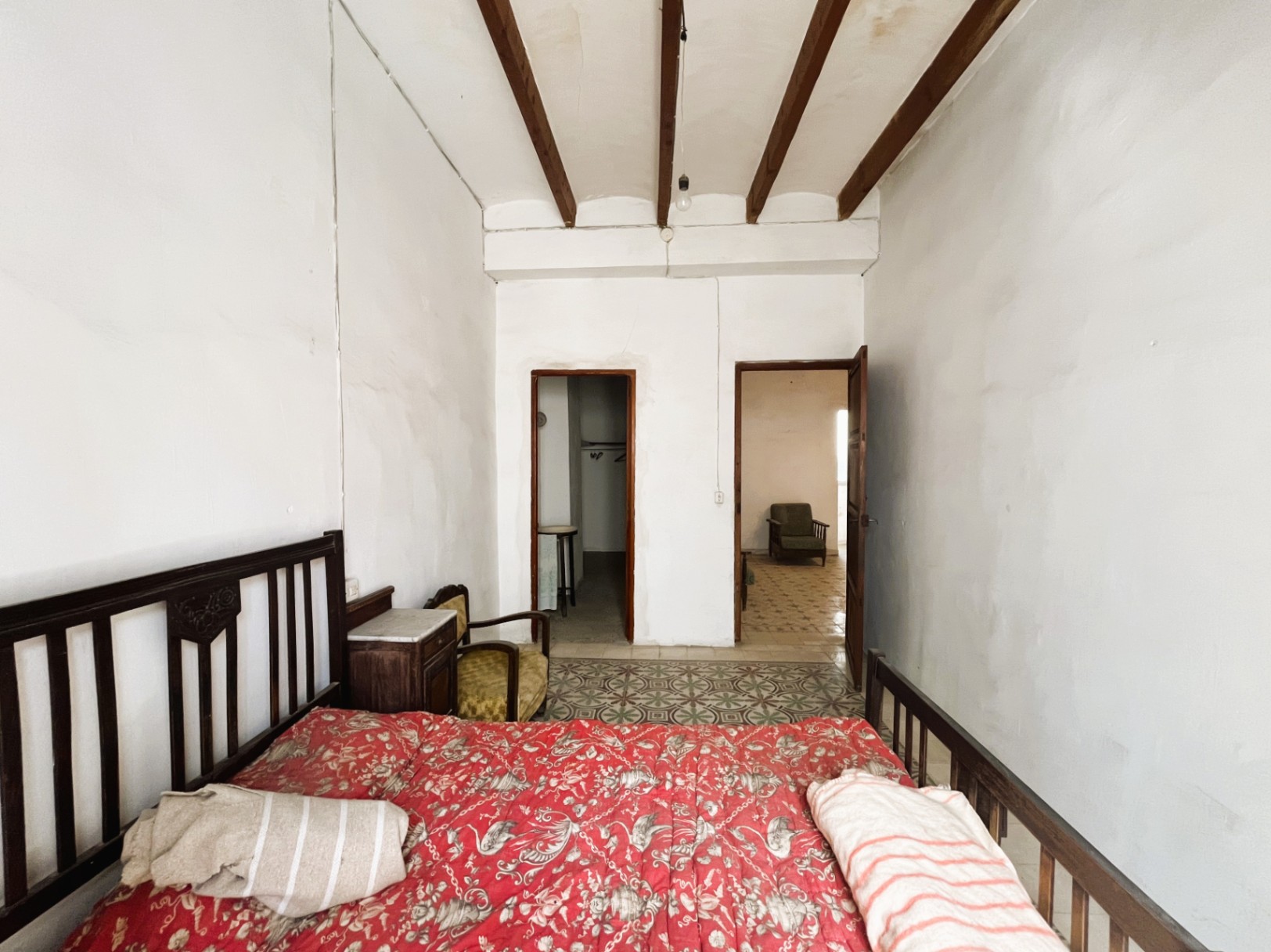 Schlafzimmer mit hohen Decken, sichtbaren Holzbalken, originalen hydraulischen Fliesenböden und antiken Möbeln mit Blick in angrenzende Räume.