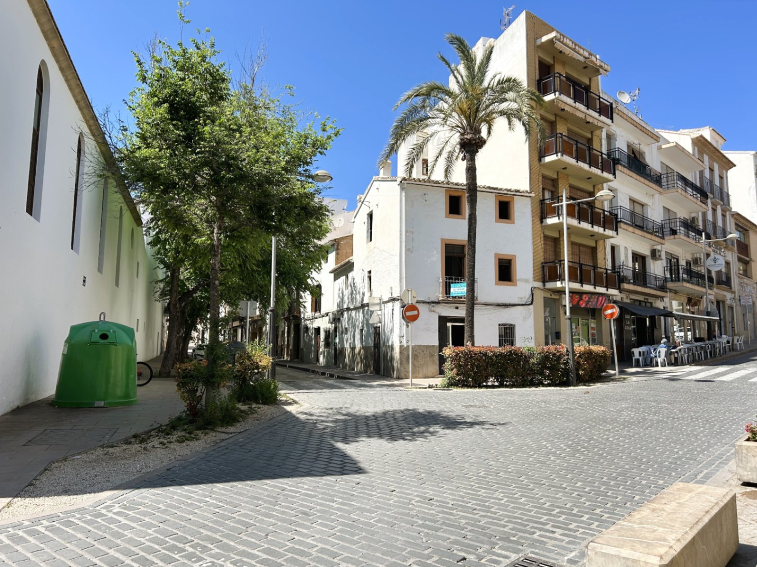 Außenansicht der weißen Eckfassade in einer gepflasterten Straße der Altstadt von Jávea, flankiert von einer Palme und traditionellen Gebäuden.
