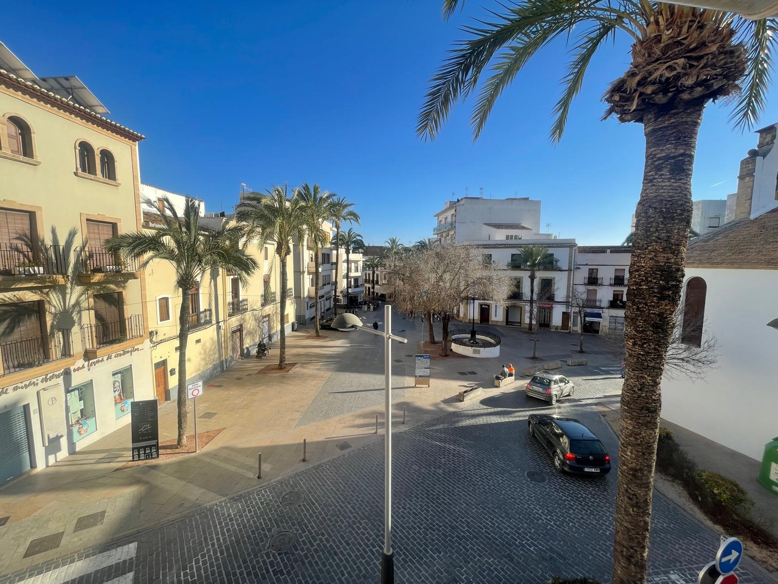 Erhöhter Blick von der Immobilie auf einen gepflasterten Platz in der Altstadt von Jávea, umgeben von traditioneller Architektur und Palmen.