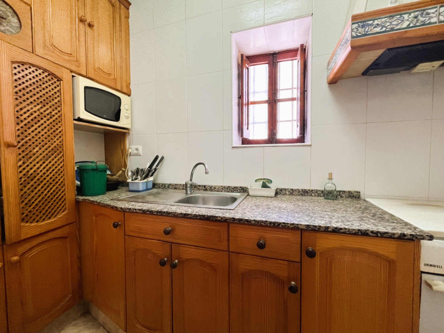 Geschlossene Küche mit traditionellen Holzschränken, Granitarbeitsplatte und einem Doppeleinspülbecken unter einem klassischen Holzfenster.