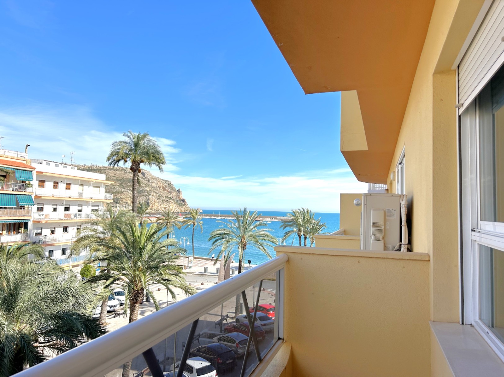 Balkon mit direktem Blick auf das Meer und den Hafen von Jávea, geprägt durch Palmen, ein Metallgeländer und weiße Außenfensterläden.