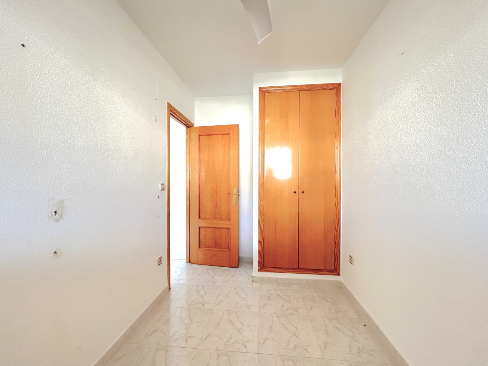 Flurbereich mit hellen Bodenfliesen in Marmoroptik, weißen Wänden und einem Einbauschrank aus Naturholz mit passender Zimmertür.