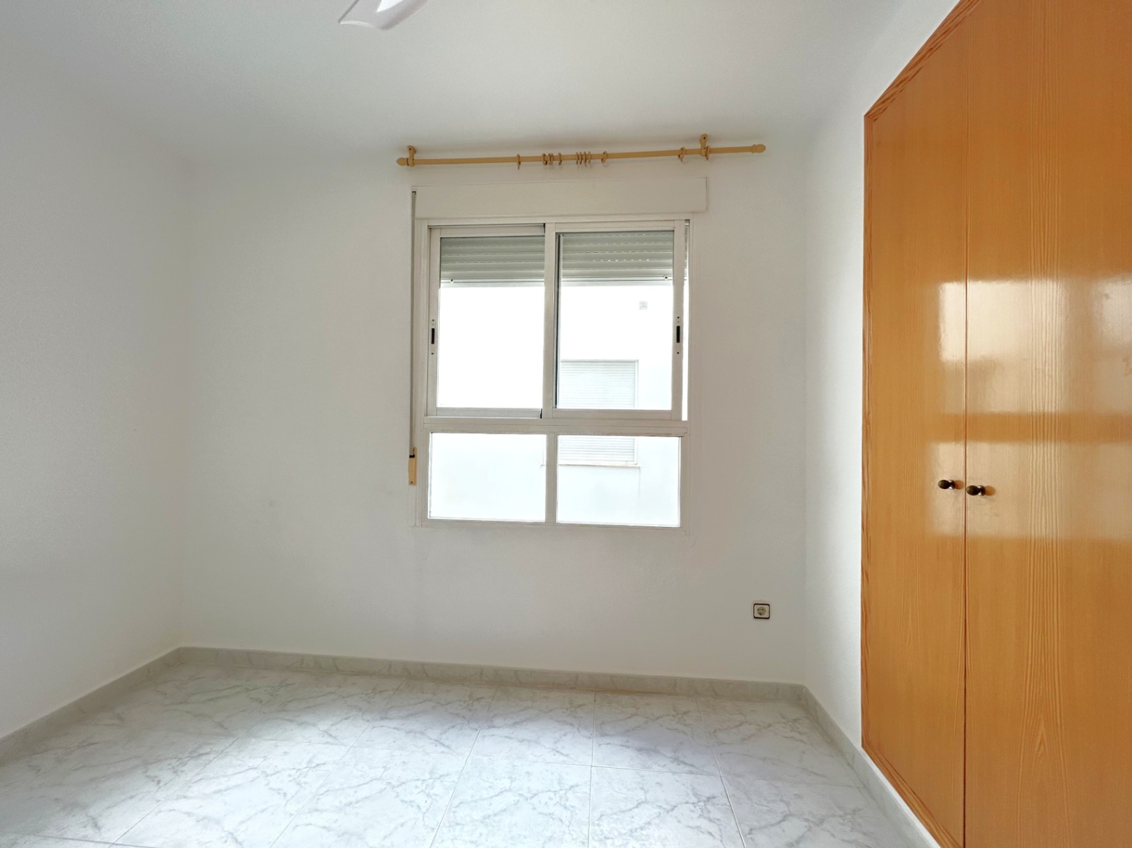Helles Schlafzimmer mit Bodenfliesen in Marmoroptik, Einbauschrank aus Holz und weißem Aluminiumfenster mit integriertem Rollladen.