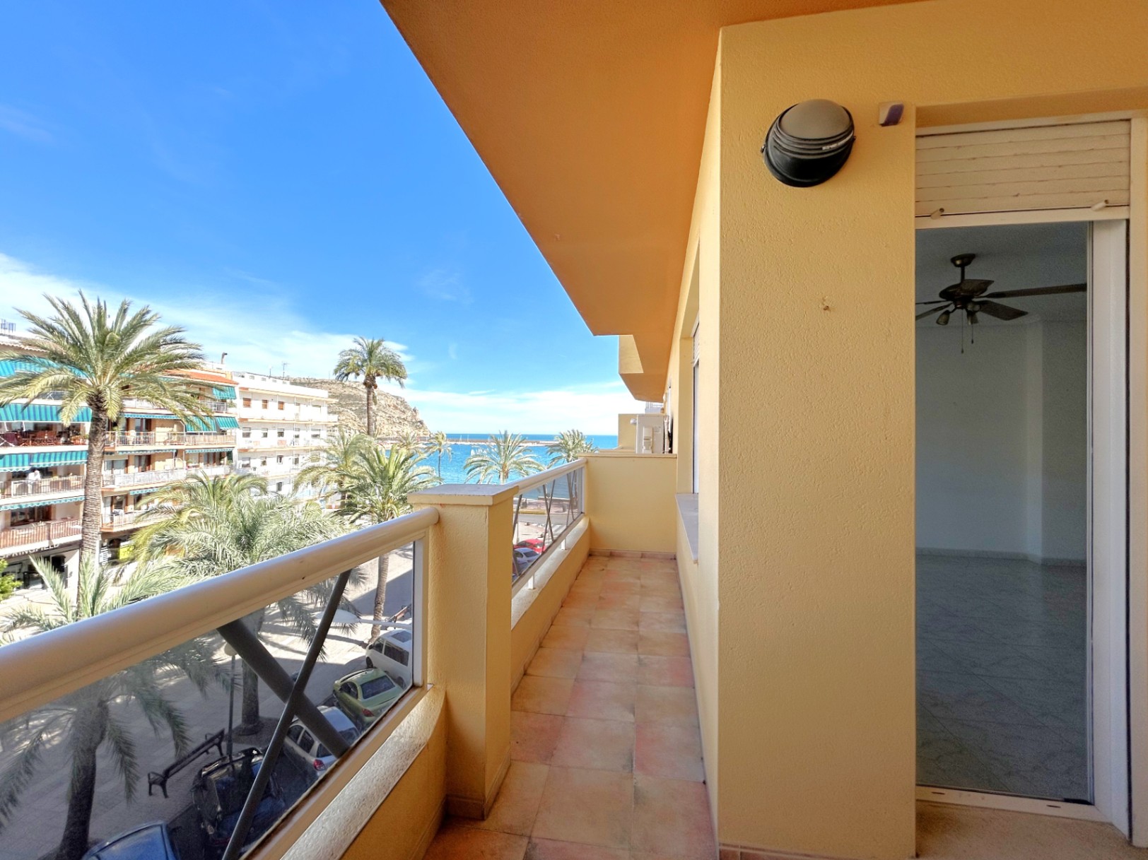 Langgestreckter Balkon mit Fliesenboden und seitlichem Blick auf das Mittelmeer und den Hafen von Jávea, umgeben von Palmen.
