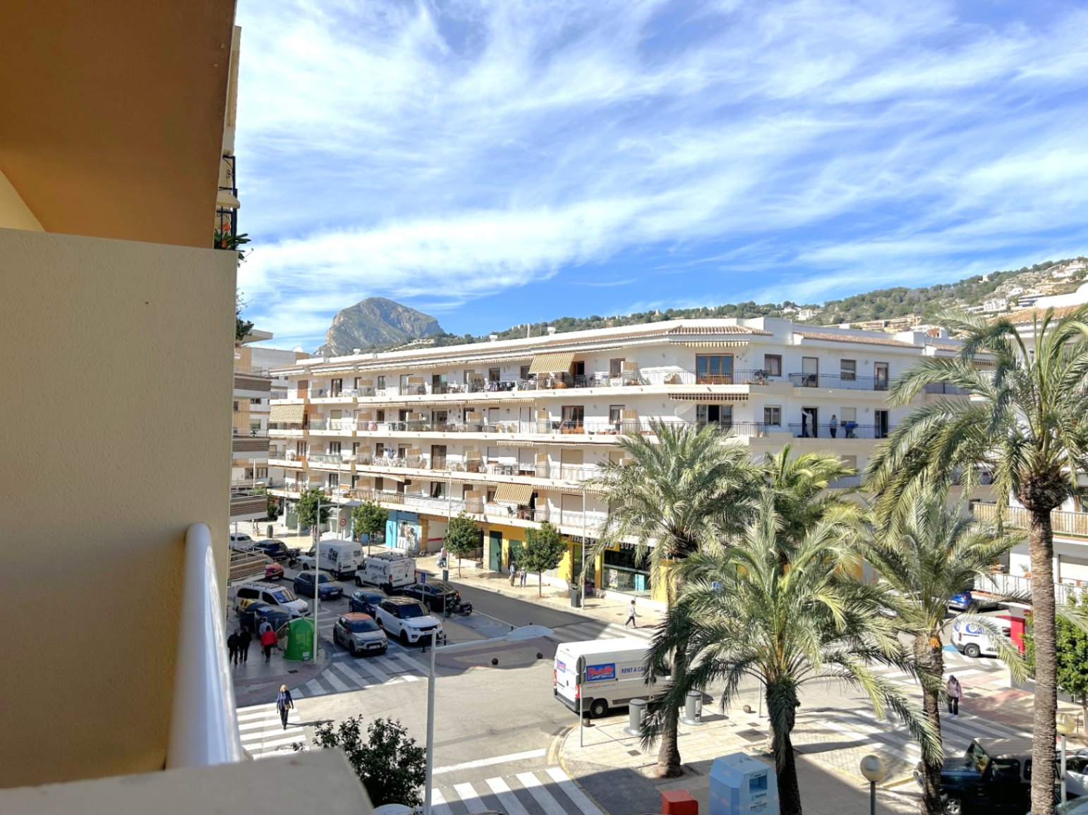 Weitläufiger Blick vom Balkon auf das Zentrum von Puerto de Jávea, mit dem markanten Berg Montgó im Hintergrund und von mediterranen Palmen gesäumten Straßen.