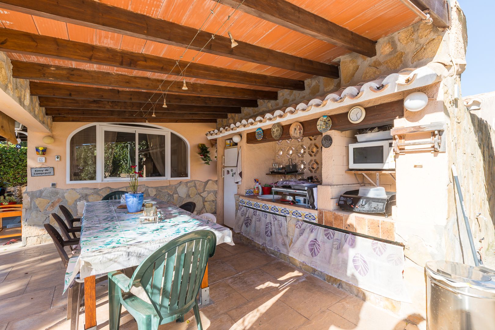 Außenküche und Essbereich unter einer Veranda mit sichtbaren Holzbalken, Natursteinwänden und einem funktionalen Grillplatz.