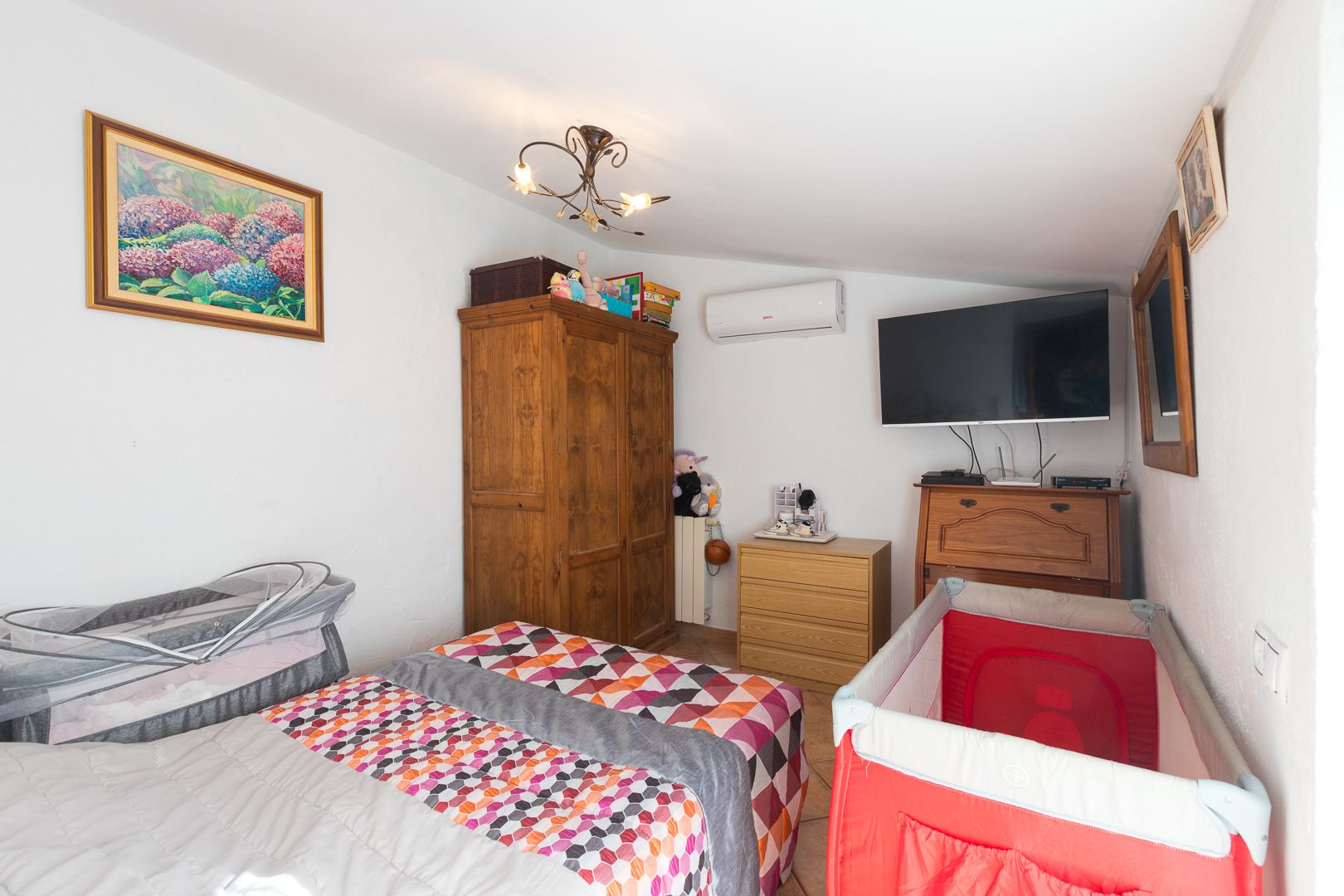 Helles Schlafzimmer mit Dachschräge, Klimaanlage, klassischen Holzmöbeln und praktischer Raumaufteilung für eine vielseitige Nutzung.