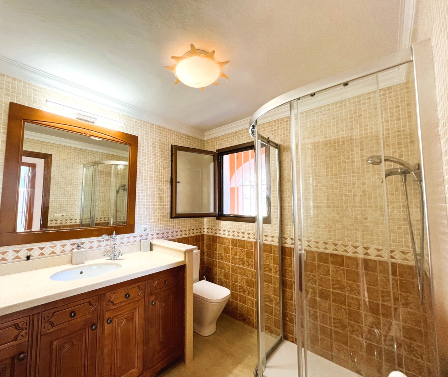 Badezimmer mit geschnitztem Holzwaschtisch, Eckdusche mit gebogener Glaswand und zweifarbigen Wandfliesen in warmen Erdtönen.