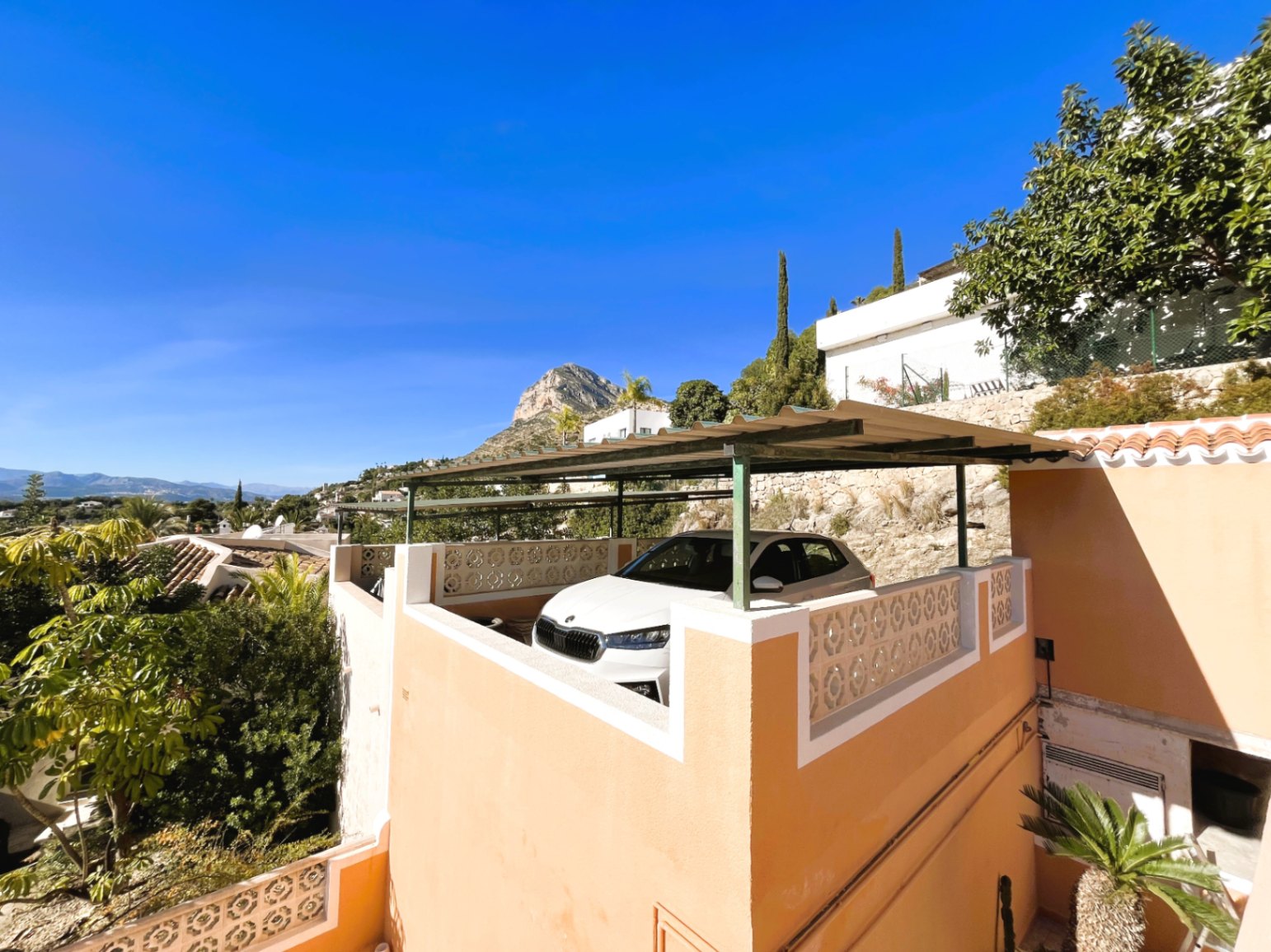 Hochgelegener Parkplatz mit Metallpergola und dekorativem Geländer, der einen freien Blick auf den Montgó und die umliegende Landschaft bietet.