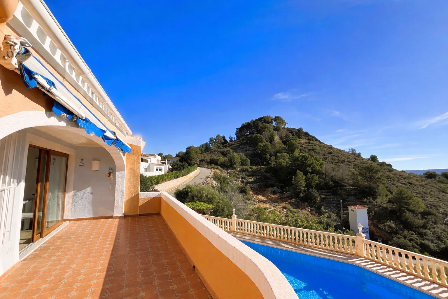 Obere Terrasse mit Terrakottafliesen, ausfahrbarer Markise und Panoramablick auf den Montgó-Hügel und den darunter liegenden Pool.