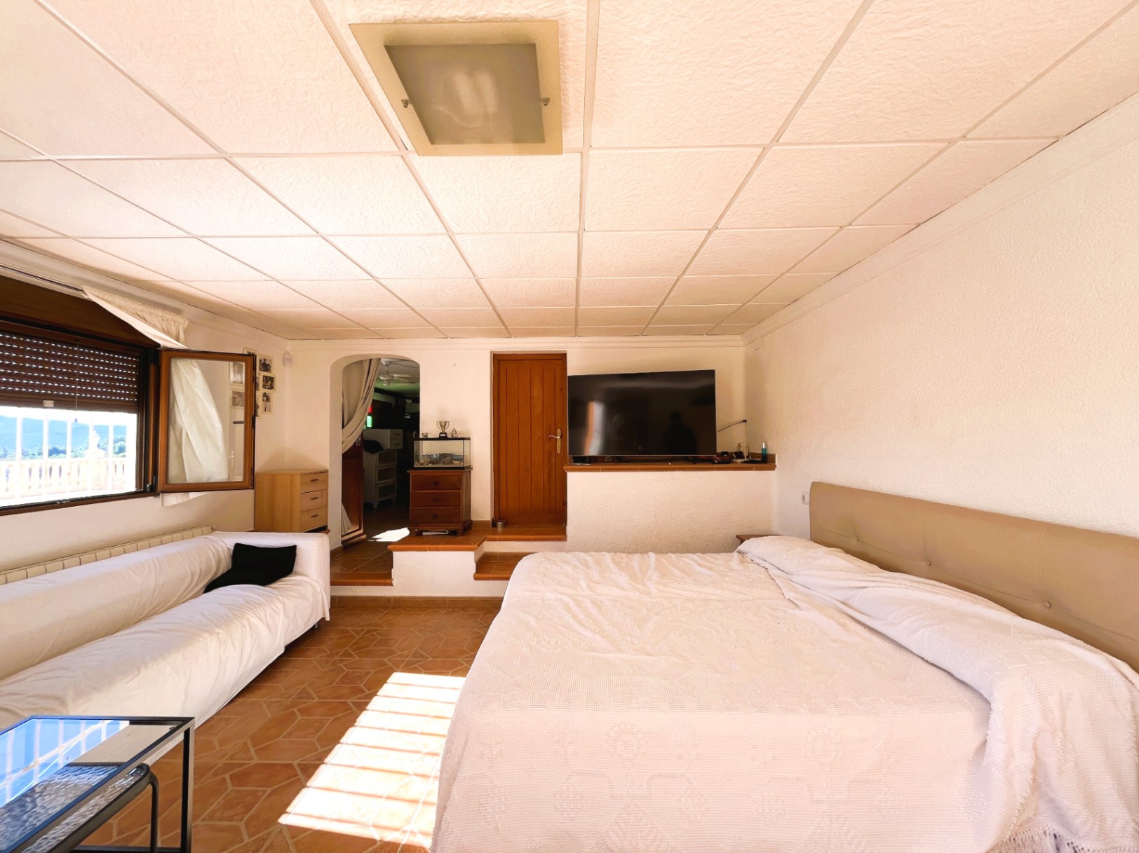 Schlafzimmer im Untergeschoss mit Terrakottafliesen, integriertem Wohnbereich und Tageslicht mit weitem Blick auf die Landschaft.