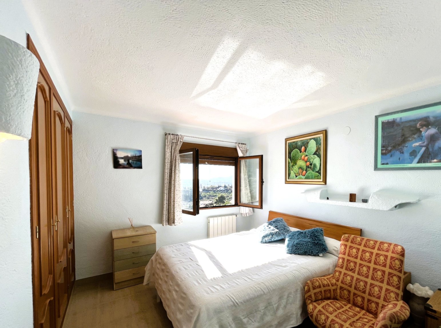 Schlafzimmer mit Einbauschränken aus Holz, Doppelbett und Fenster mit Panoramablick auf das Tal, geprägt von hellem, natürlichem Tageslicht.