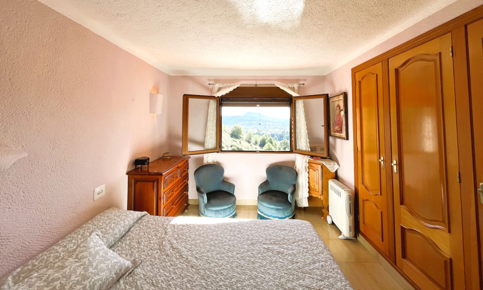 Schlafzimmer mit malvenfarbenen Wänden, Holz-Einbauschränken und Fenster mit weitem Panoramablick auf das Tal und die umliegende Natur.