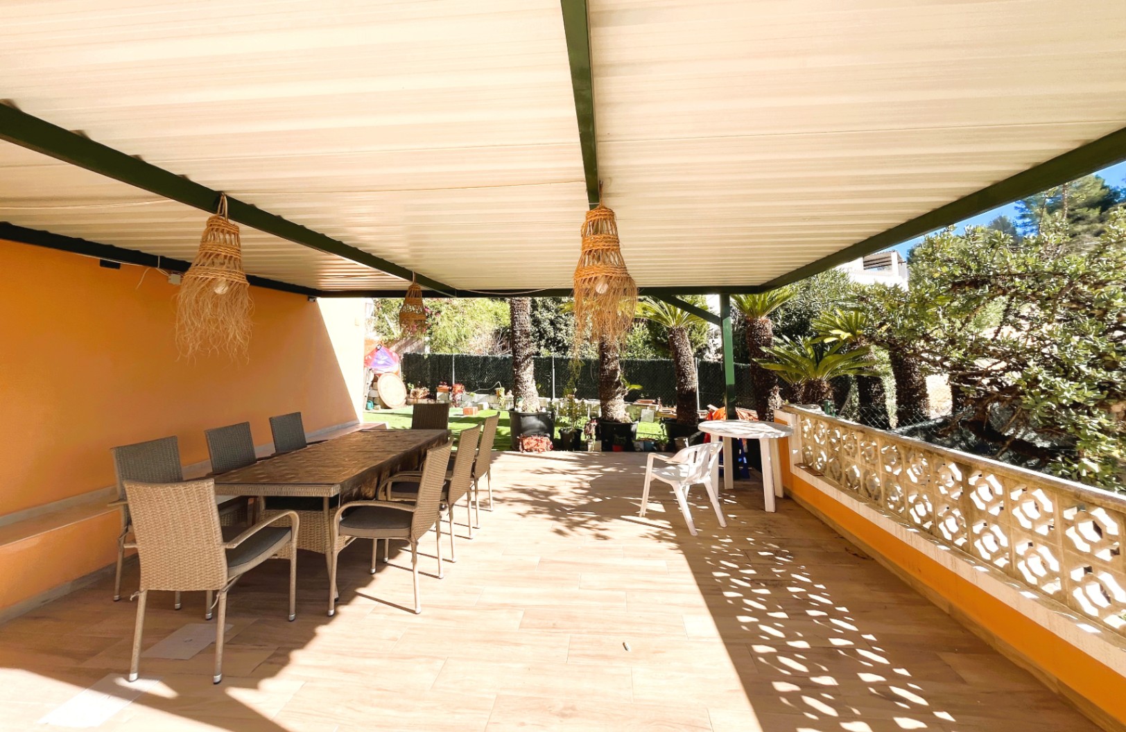 Überdachte Terrasse mit Essbereich im Freien, Korblampen und dekorativer Balustrade mit Blick auf den mediterranen Garten.