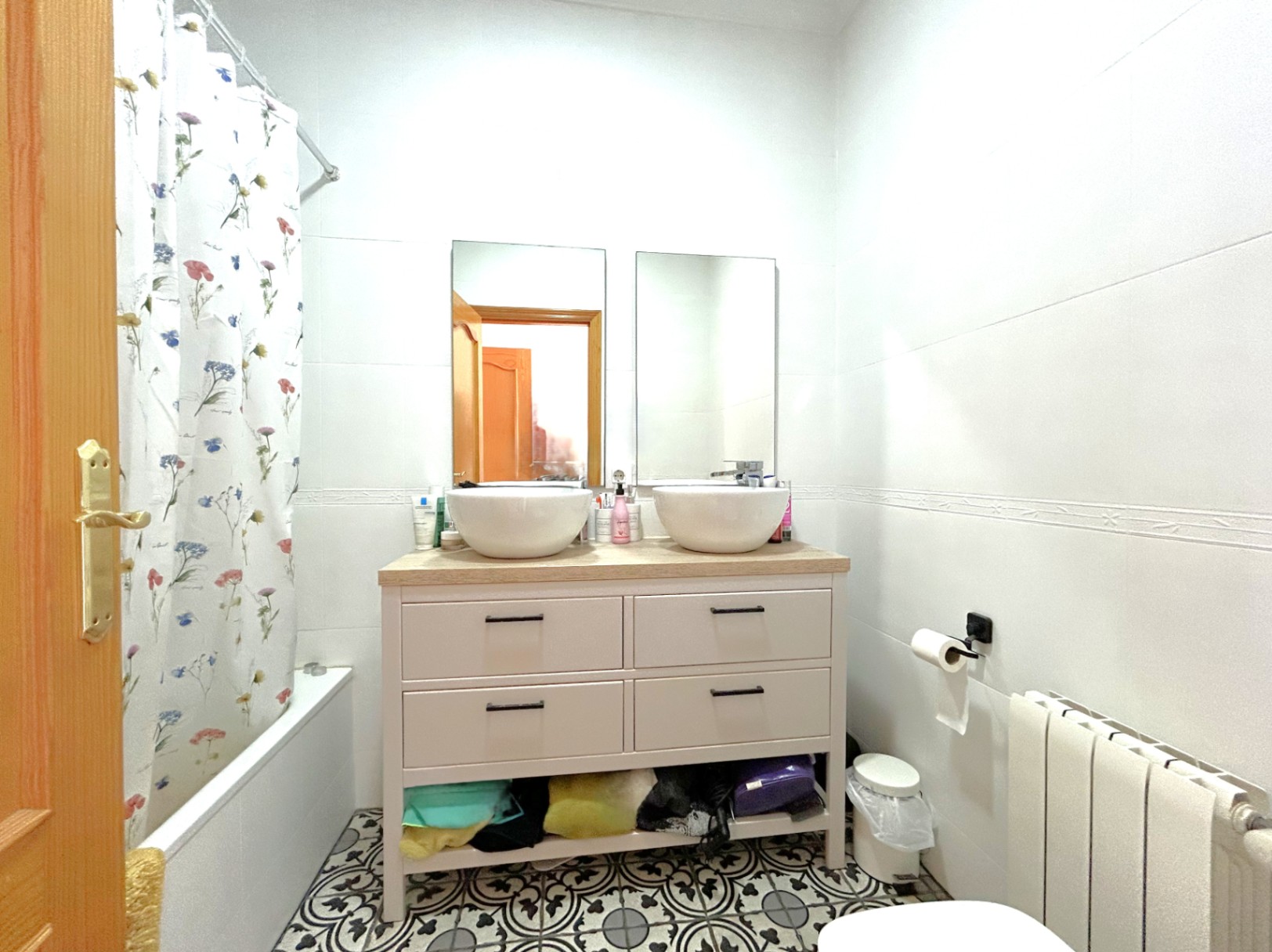 Badezimmer mit Doppelwaschtisch auf Holzplatte, dekorativen hydraulischen Bodenfliesen, Badewanne und Zentralheizungskörper.