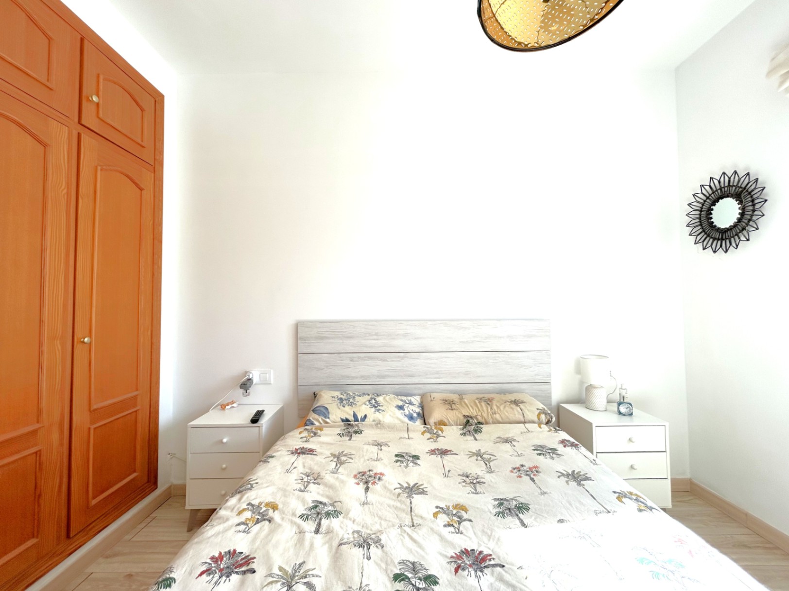 Doppelzimmer mit Einbauschrank aus Holz, weißen Nachttischen und einem hellen Holzkopfteil. Der Raum ist mit Laminatboden ausgestattet und bietet viel natürliches Licht.