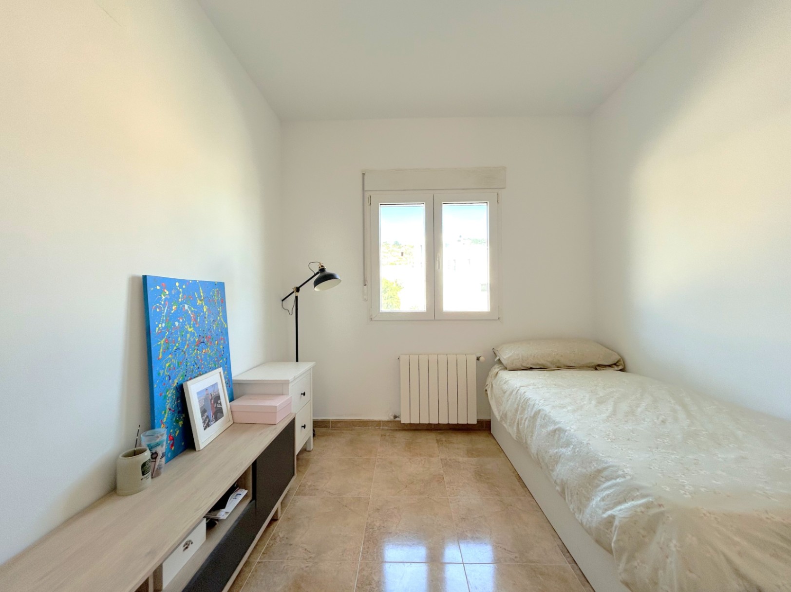 Helles Schlafzimmer mit Fliesenboden, Zentralheizungsradiator und doppelt verglastem Fenster für reichlich natürliches Licht.