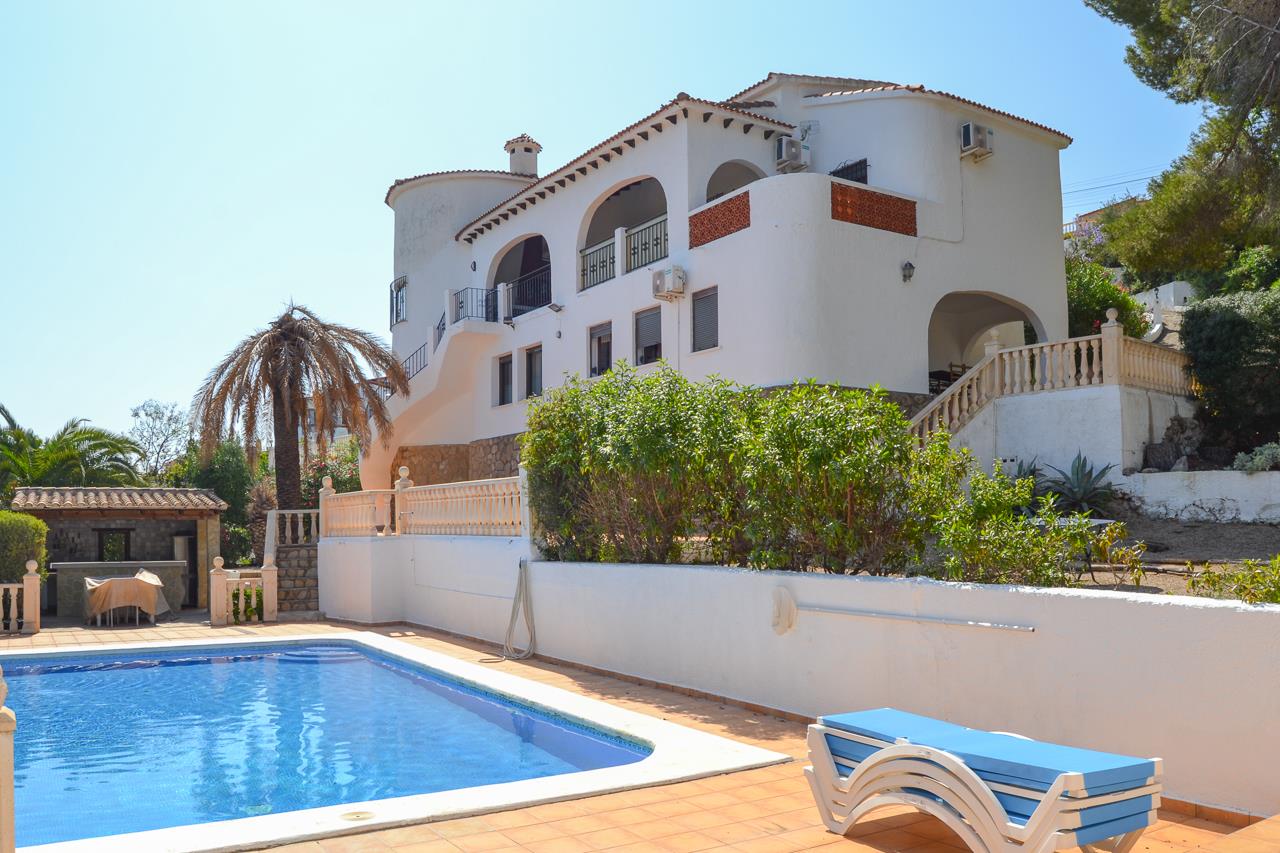 Außenansicht der weißen Villa mit großem Pool, sonnigen Terrassen und mediterraner Architektur mit Rundbögen und Natursteinelementen.