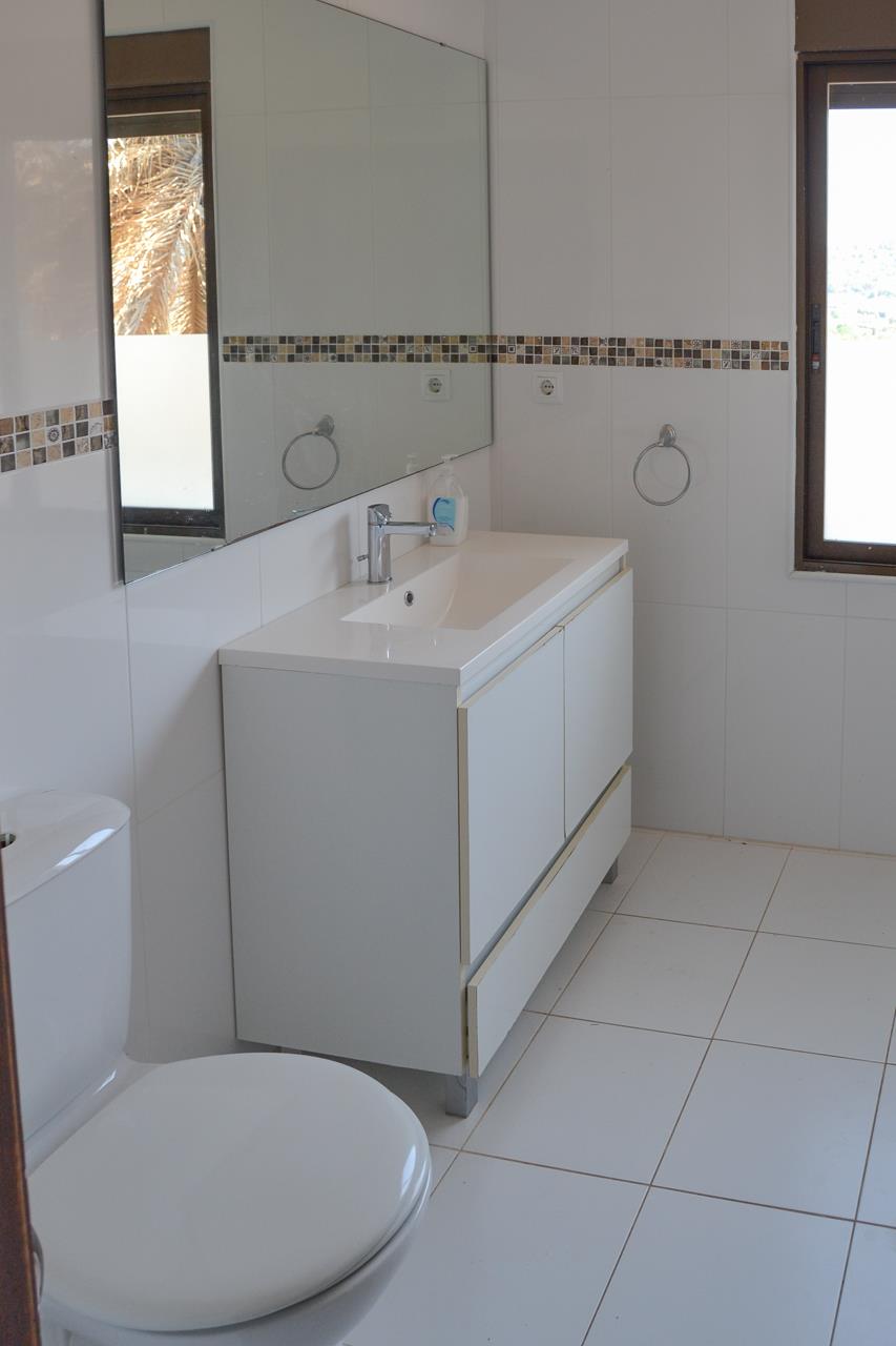 Badezimmer mit weißem Waschtisch, großem Spiegel und gefliesten Wänden mit Mosaikbordüre. Mit natürlichem Licht durch das Fenster und hellem Keramikboden.