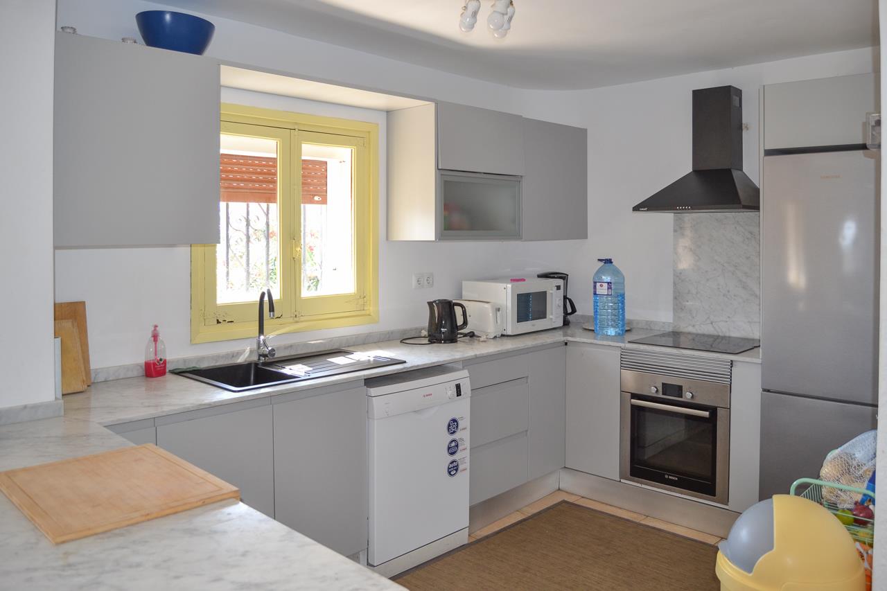 Funktionale Küche mit grauen Schränken, Arbeitsplatten in Marmoroptik und Einbaugeräten. Ausgestattet mit Geschirrspüler, Backofen und einem gelb gerahmten Fenster.