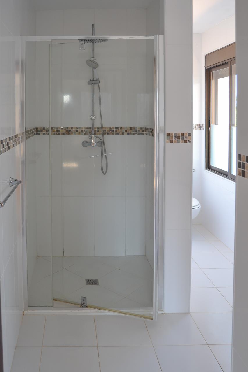 Funktionelles Badezimmer mit Glasdusche, weißen Wandfliesen und dekorativer Mosaikbordüre in Erdtönen sowie hellem, natürlichem Lichteinfall.