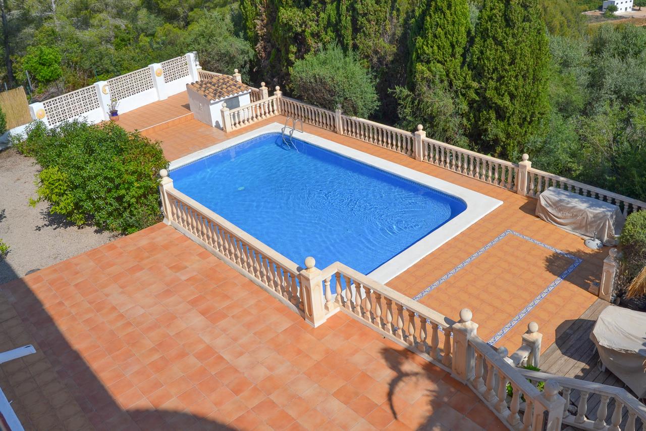 Großer rechteckiger Pool mit weißer Steineinfassung, umgeben von einer Terrakotta-Terrasse und einer klassischen Steinbalustrade inmitten mediterraner Vegetation.
