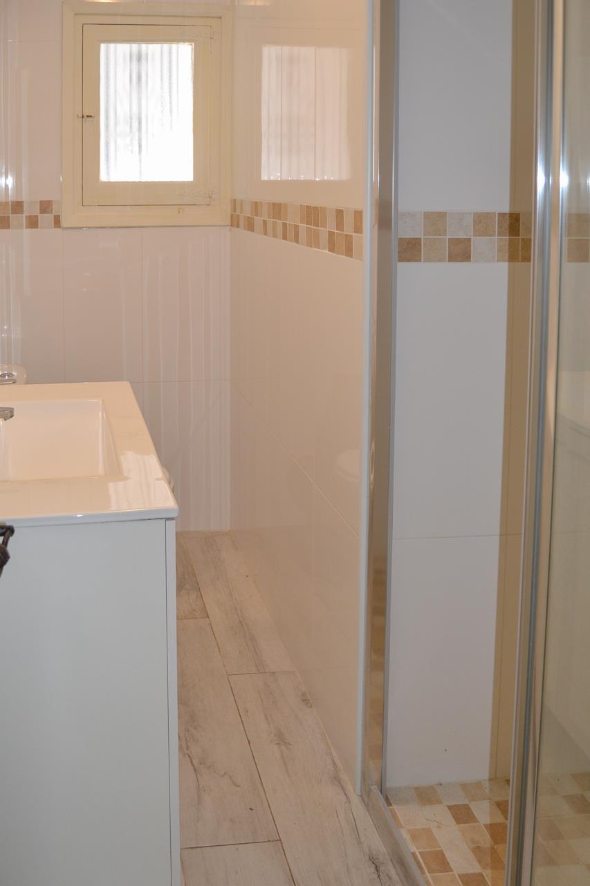 Modernes Badezimmer mit weißem Waschtisch, gefliesten Wänden mit Mosaikbordüre und einer Glasduschkabine mit passendem Mosaikboden.