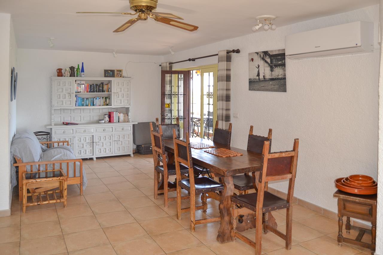 Rustikaler Essbereich mit massivem Holztisch, Hochlehner-Stühlen, weißem Sideboard und Fliesenboden. Ausgestattet mit Klimaanlage, Deckenventilator und Terrassenzugang.