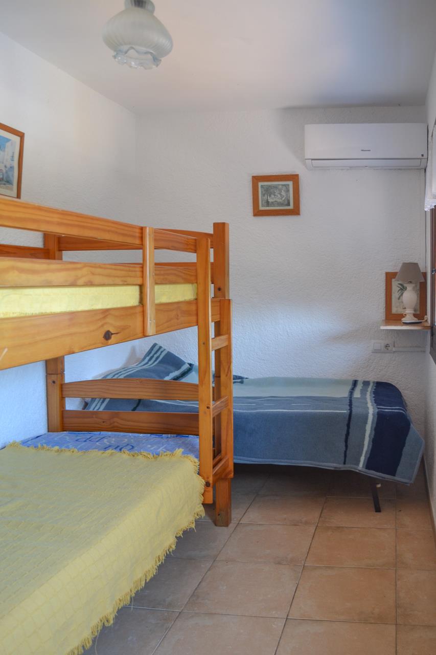 Schlafzimmer mit Etagenbetten aus Kiefernholz und einem Einzelbett, ausgestattet mit Klimaanlage, Fliesenboden und strukturierten weißen Wänden.