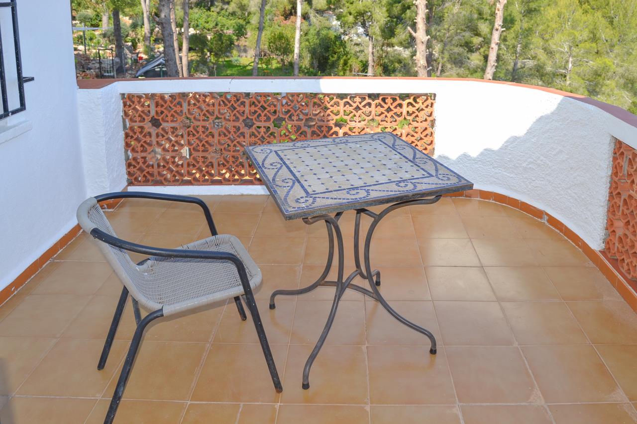 Terrasse mit Terrakotta-Fliesen, einem blauen Mosaiktisch und einer dekorativen Gitterbrüstung aus Keramik mit Blick auf die umliegenden Pinien.