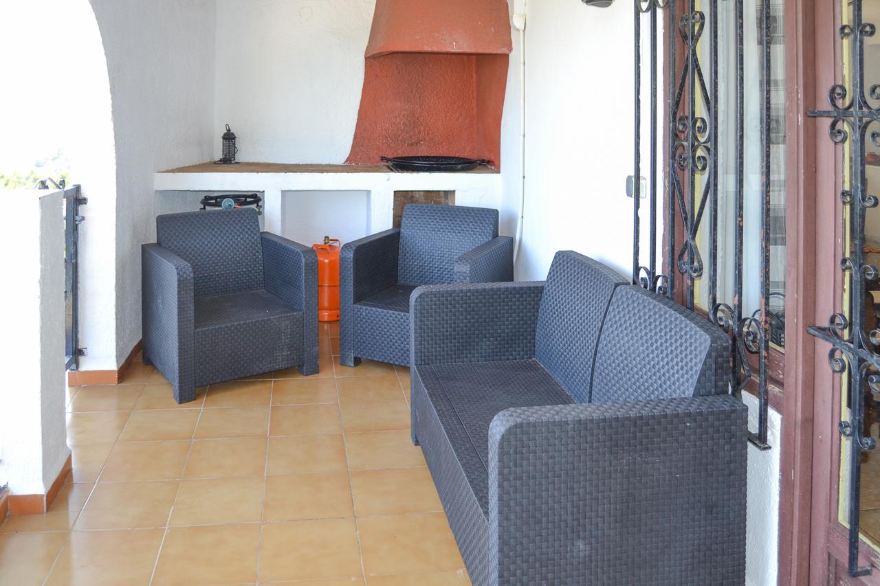 Überdachte Terrasse mit dunklen Rattansitzmöbeln, Terrakotta-Fliesenboden und integriertem Grillkamin mit markanter rötlicher Abzugshaube.