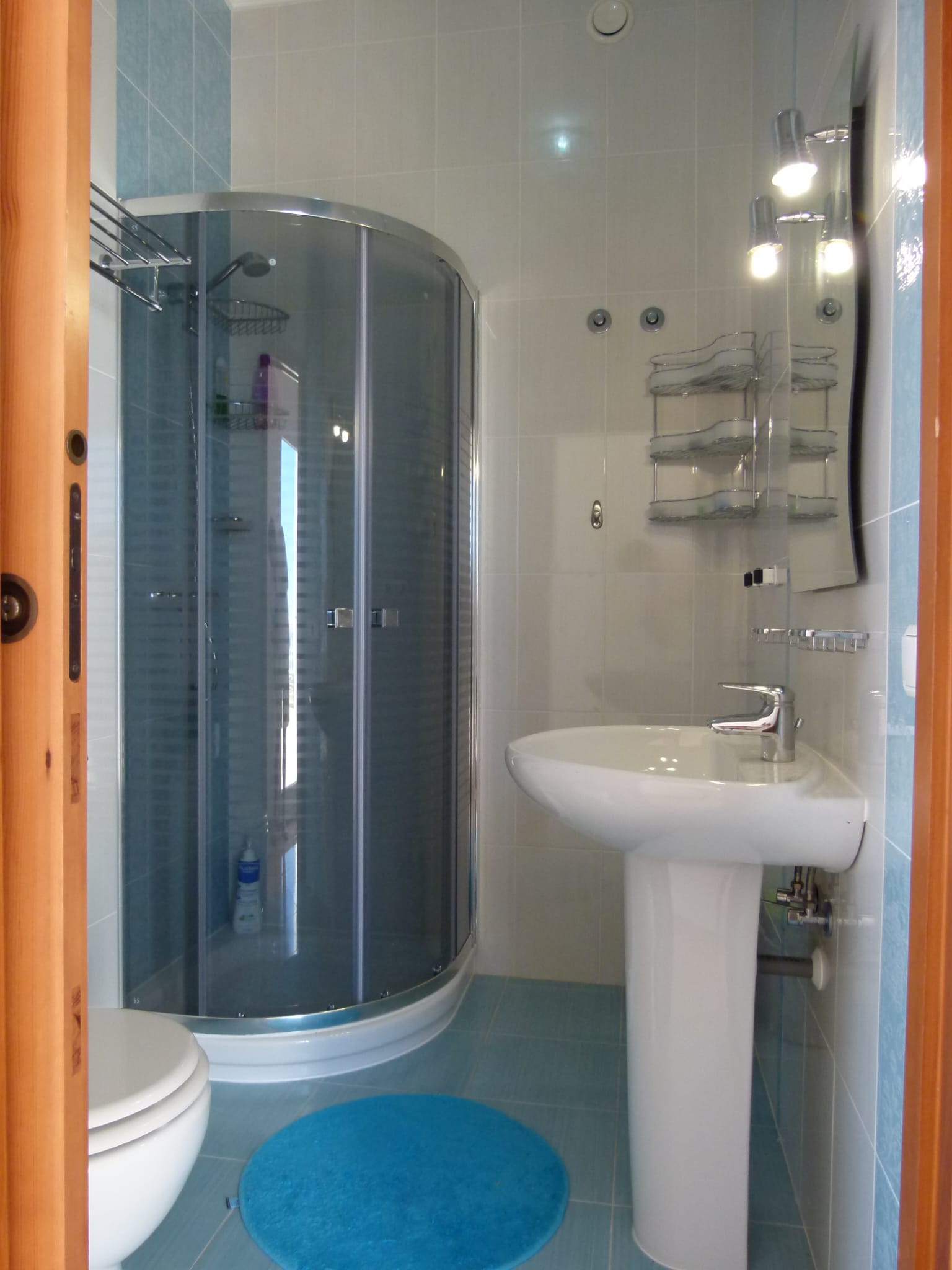 Badezimmerdetail mit Eckdusche, Waschtisch und blauen Fliesenakzenten.