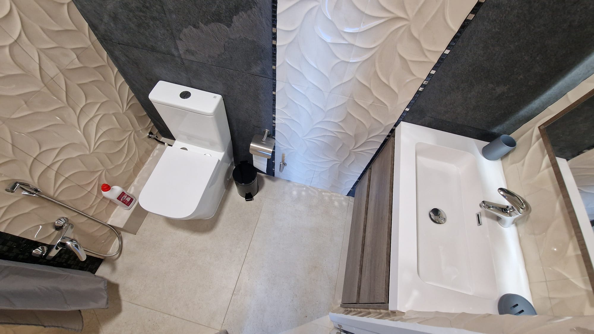 Badezimmerdetail mit strukturierten Fliesen, einer weißen Toilette und einem modernen Waschbecken. Funktionales, elegantes Design.