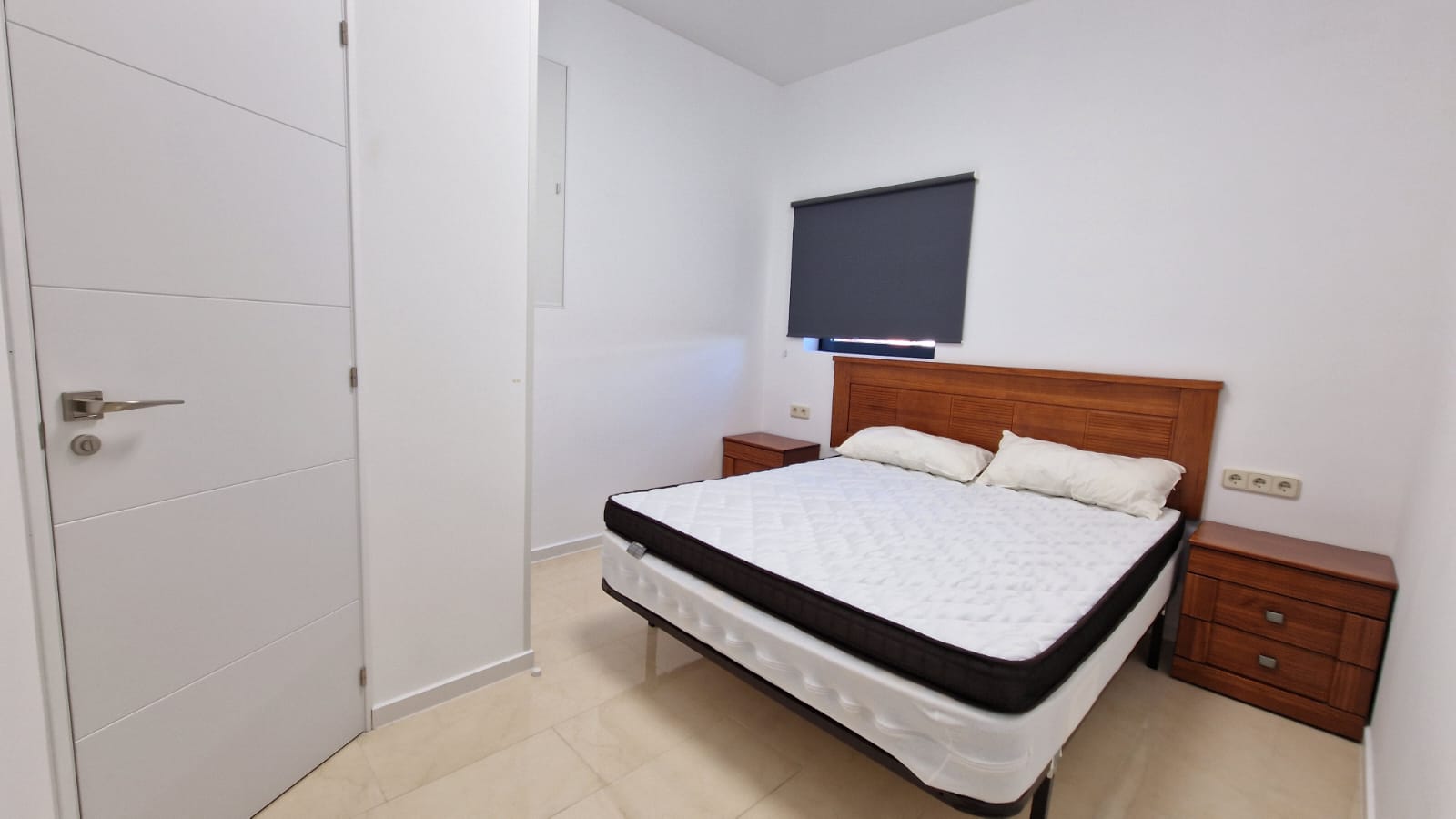 Helles Schlafzimmer mit Doppelbett, hölzernen Nachttischen und moderner weißer Tür.