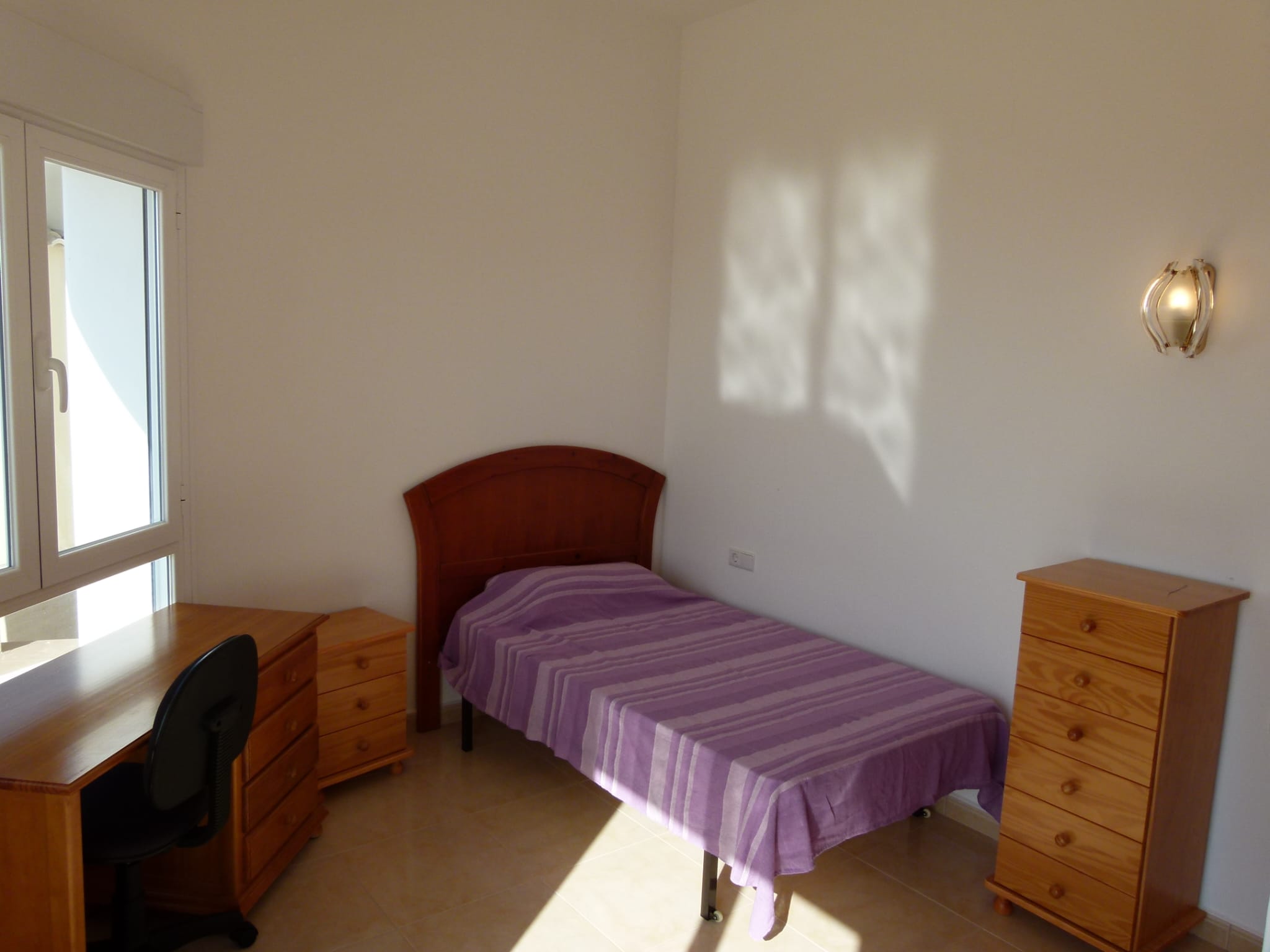 Helles Schlafzimmer mit Einzelbett, Holzschreibtisch und passender Kommode.