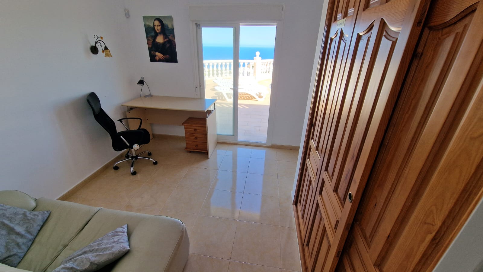 Helles Zimmer mit Schreibtisch, Holzschrank und Zugang zur Terrasse mit Meerblick.